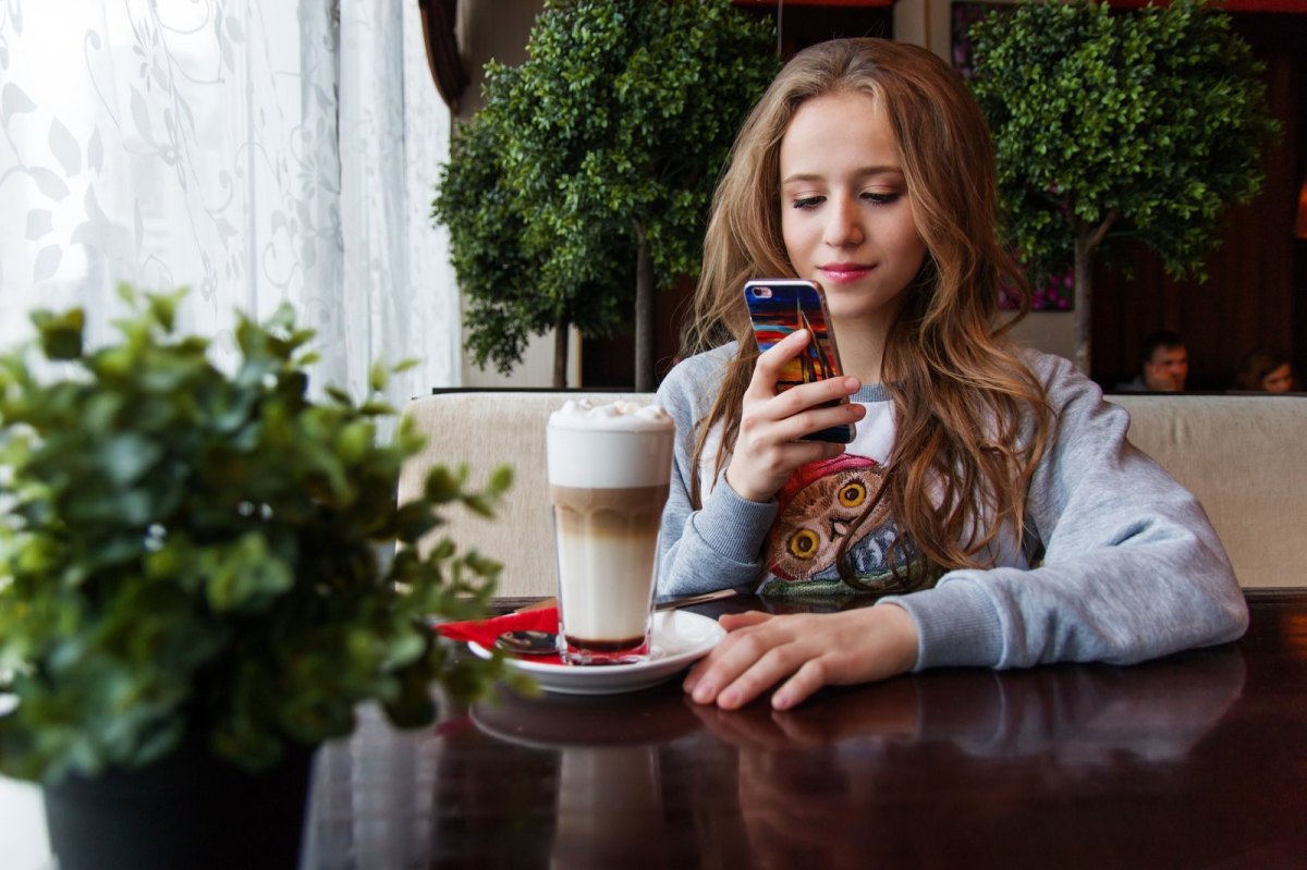 Eine Frau sitzt in einem Café und benutzt ihr Smartphone.