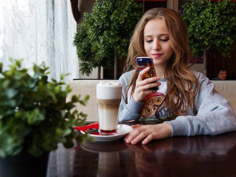 Eine Frau sitzt in einem Café und benutzt ihr Smartphone.