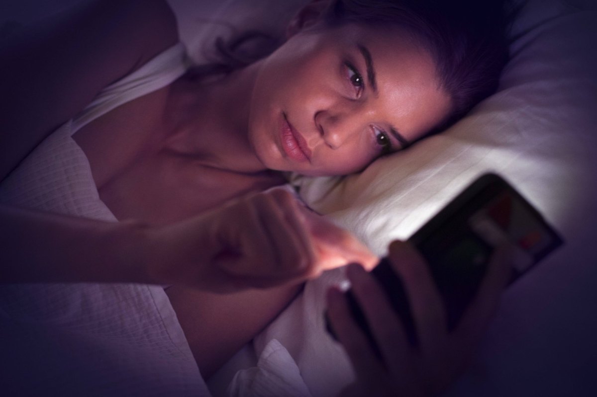 Eine Frau liegt im Bett und schaut auf ihr Smartphone.
