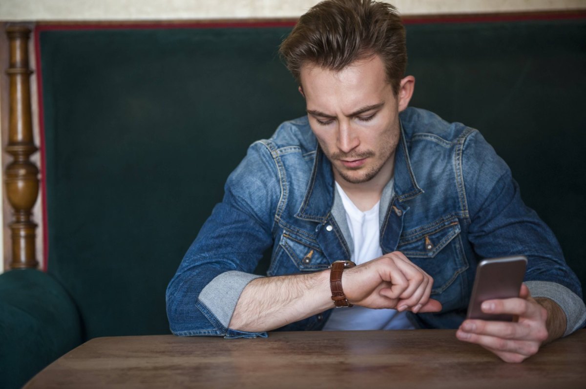 Ein Mann hält ein Smartphone in der Hand und schaut auf seine Armbanduhr