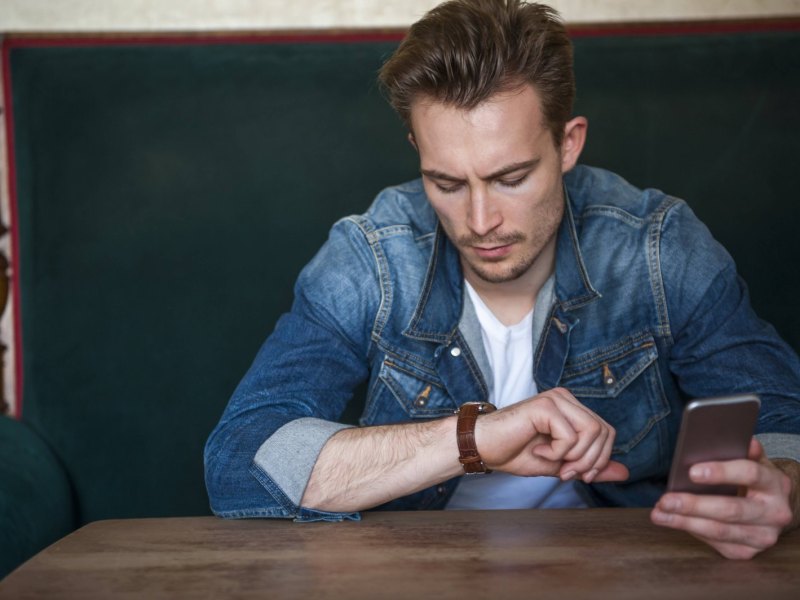 Ein Mann hält ein Smartphone in der Hand und schaut auf seine Armbanduhr