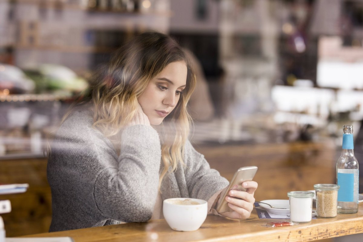 Eine Frau sitzt in einem Café und schaut auf ein Smartphone