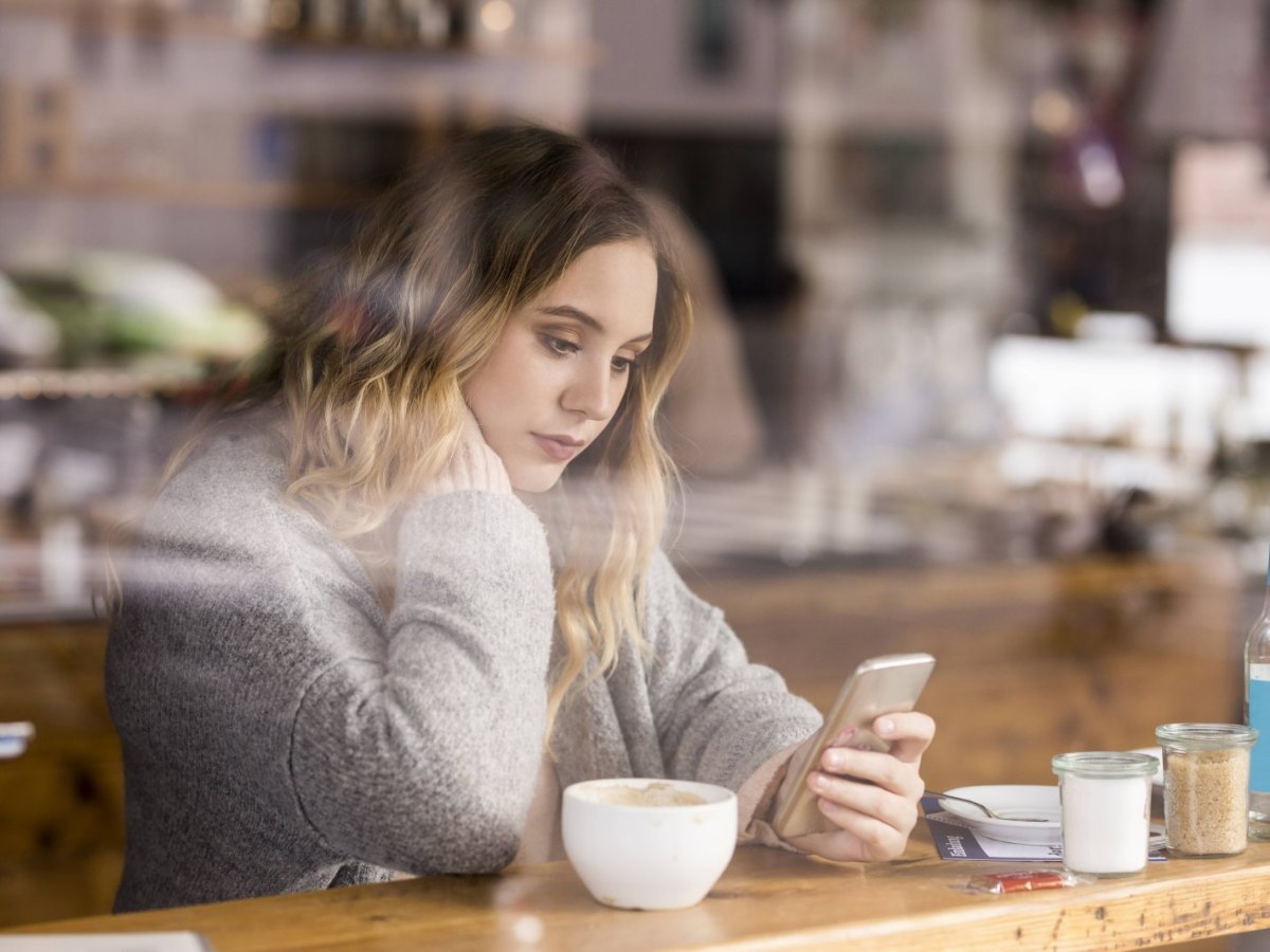 Eine Frau sitzt in einem Café und schaut auf ein Smartphone