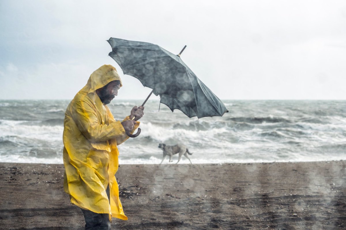 Mann in Regelmantel und Starkregen am Strand.