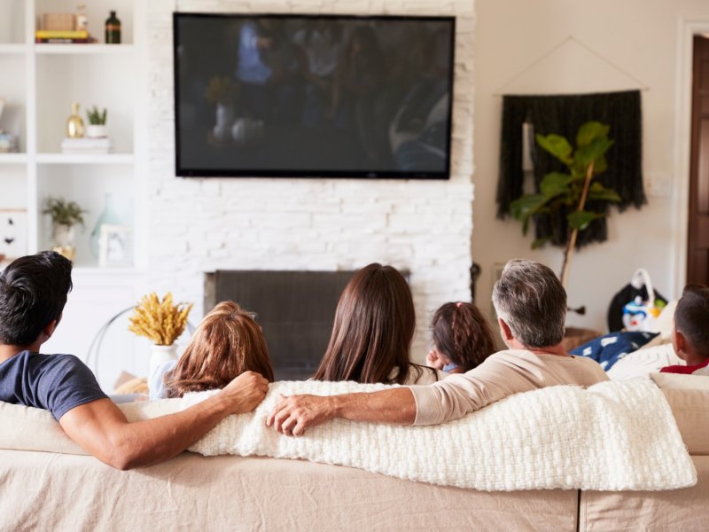 Familie sitzt vor einem Fernseher auf dem Sofa