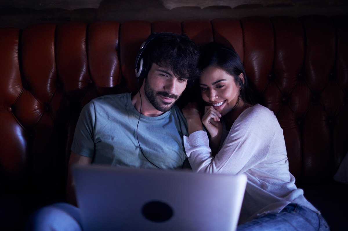 Mann und Frau sitzen mit Kopfhörern vor dem Laptop.