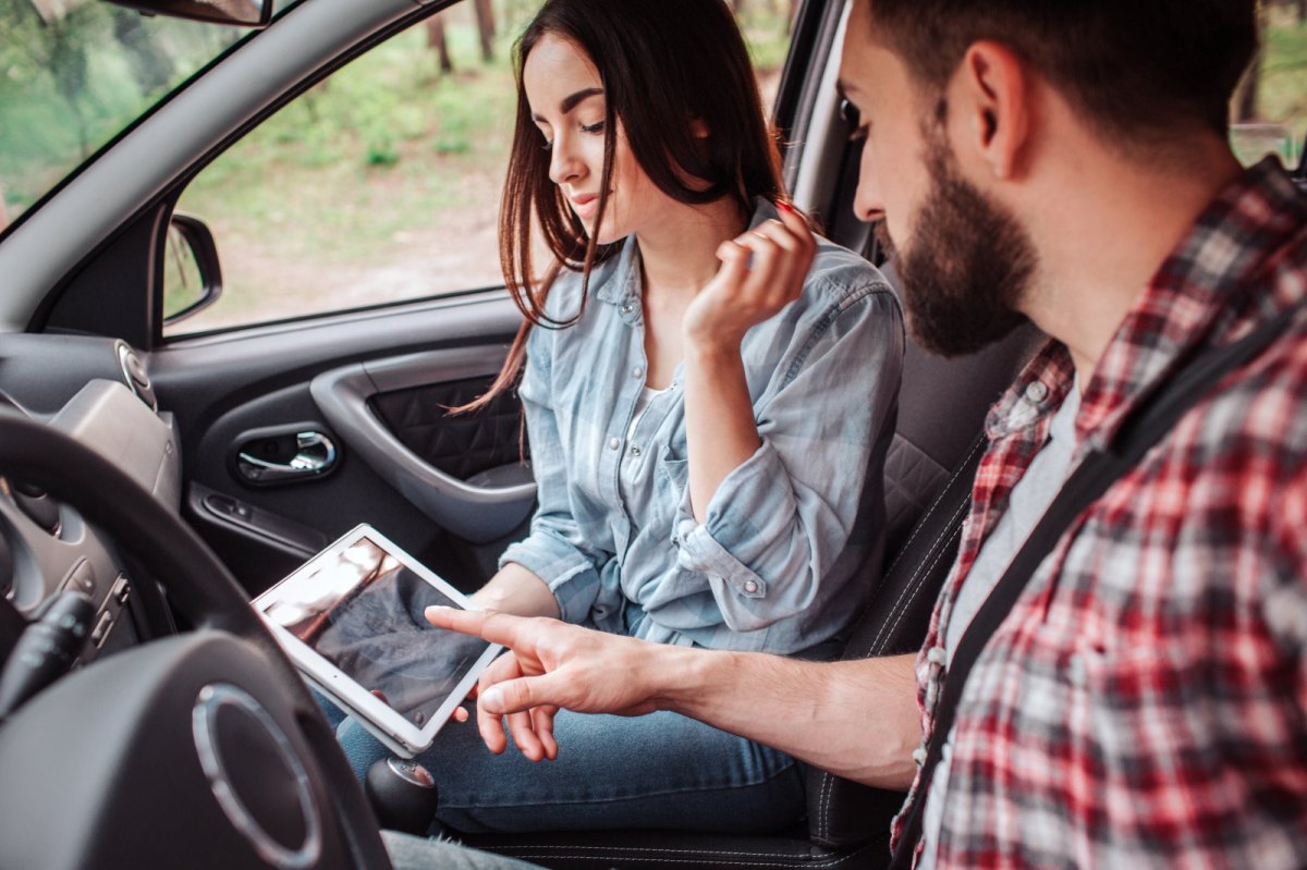 Mann und Frau sitzen mit Tablet im Auto