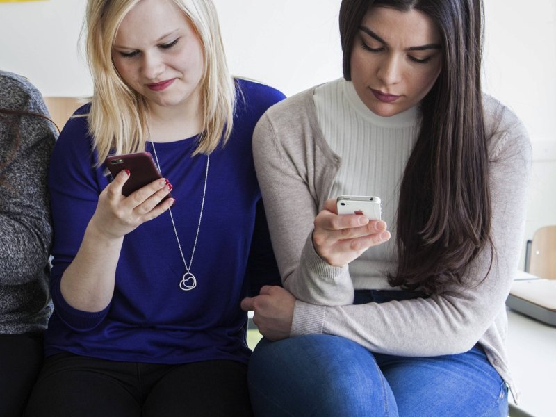 Teenage-Mädchen tippen in einem Klassenraum auf ihren Handys.