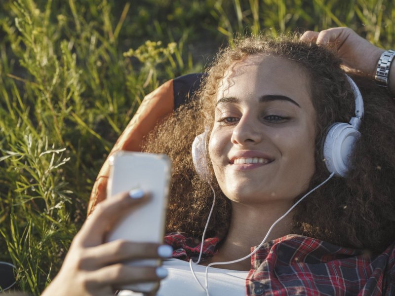 Teenager-Mädchen liegt im Gras und hört mit seinem Smartphone Musik.