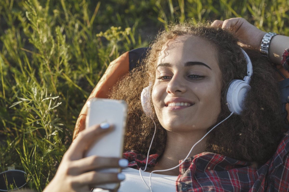 Teenager-Mädchen liegt im Gras und hört mit seinem Smartphone Musik.