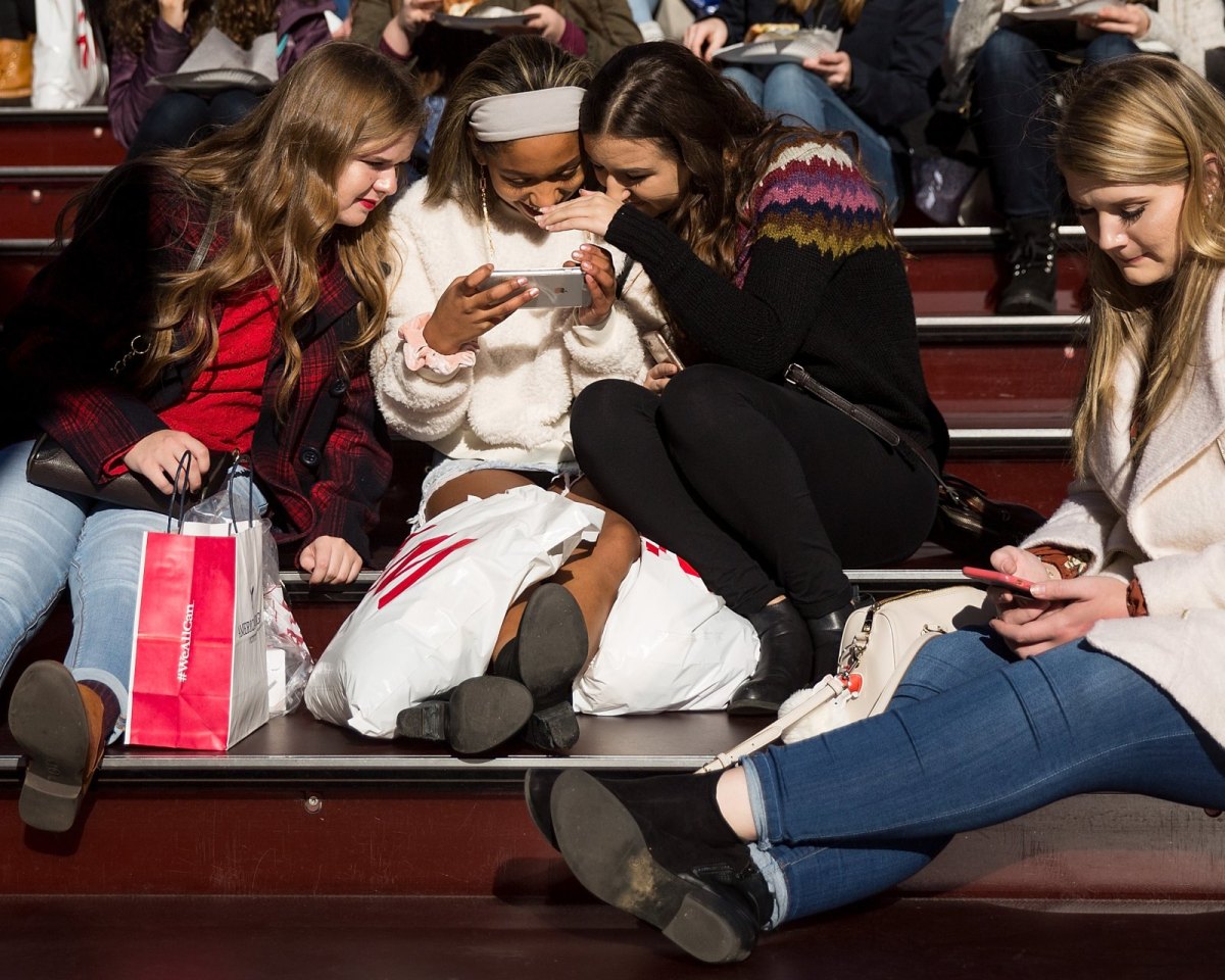 Teenager-Mädchen in einem Stadion lachen über etwas auf einem Handy.