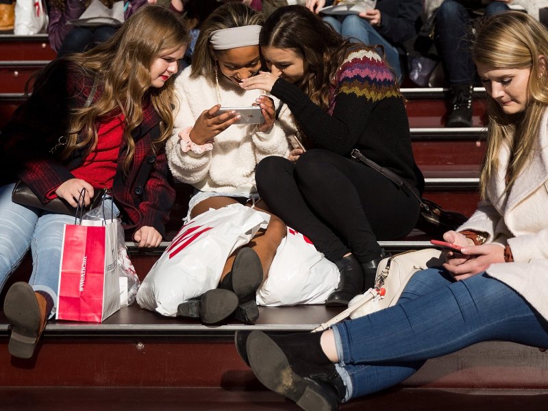 Teenager-Mädchen in einem Stadion lachen über etwas auf einem Handy.