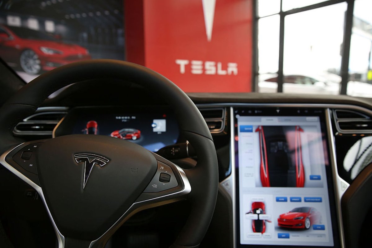 Ein Lenkrad in einem Tesla-Auto mit Logo im Hintergrund.