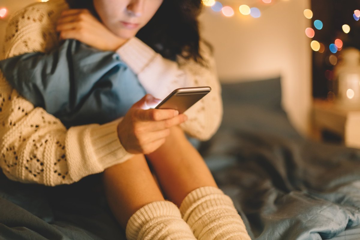 Frau sitzt mit Handy im Bett