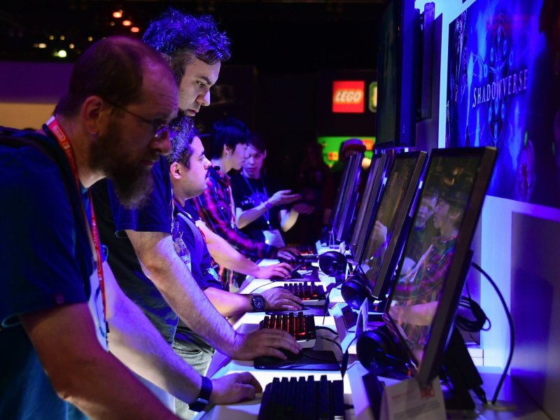 Mehrere Männer stehen je an einem Rechner nebeneinander und spielen ein Videospiel
