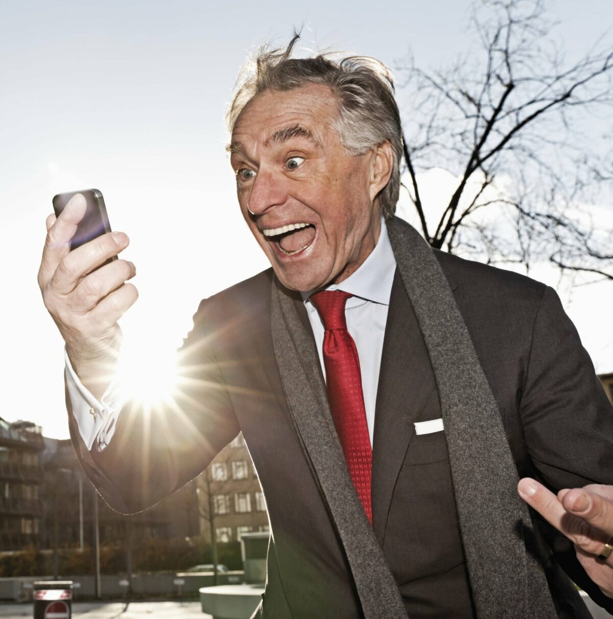 Älterer Herr im Anzug starrt begeistert auf sein Smartphone.
