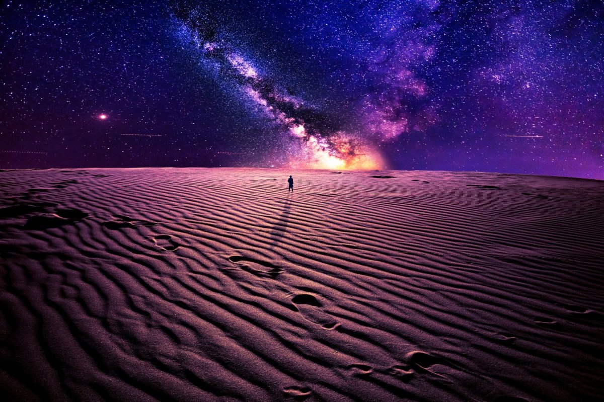 Mensch steht im Sand und blickt auf das Universum.