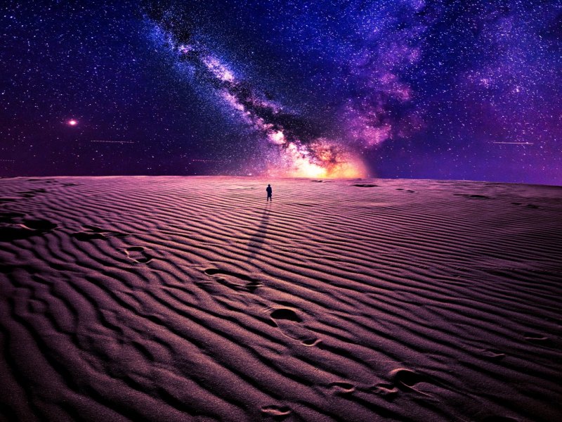 Mensch steht im Sand und blickt auf das Universum.