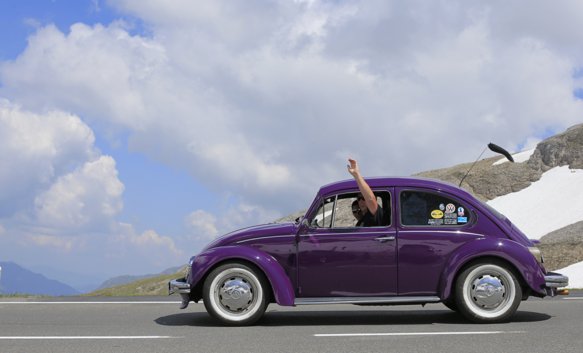 VW Käfer in lila mit winkendem Fahrer