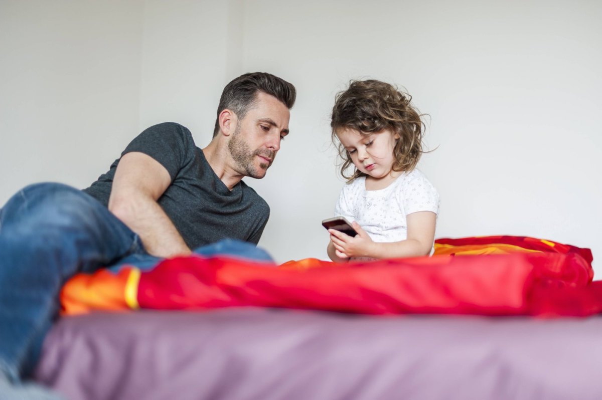Ein Vater und seine kleine Tochter gucken auf ein Smartphone