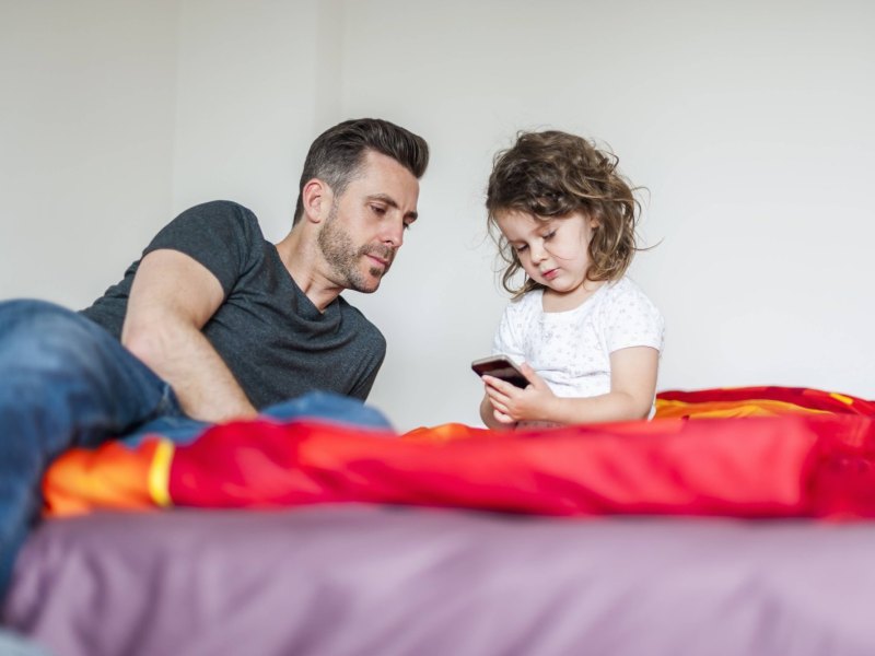 Ein Vater und seine kleine Tochter gucken auf ein Smartphone