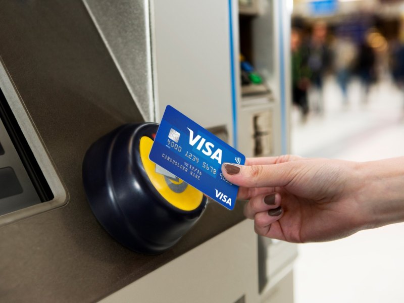 Frau bezahlt mit Visa Karte an einem Ticketautomaten.