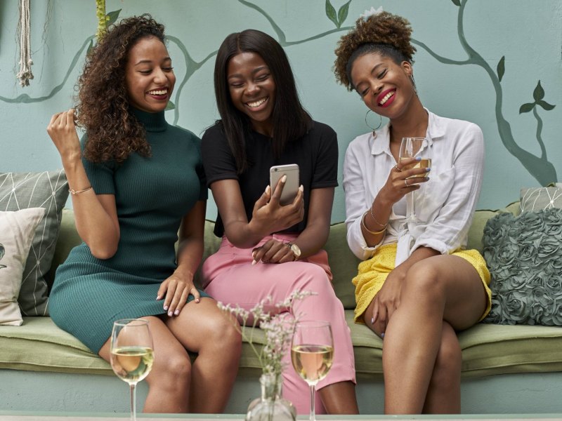 Drei Frauen trinken Wein und schauen auf ein Handy.