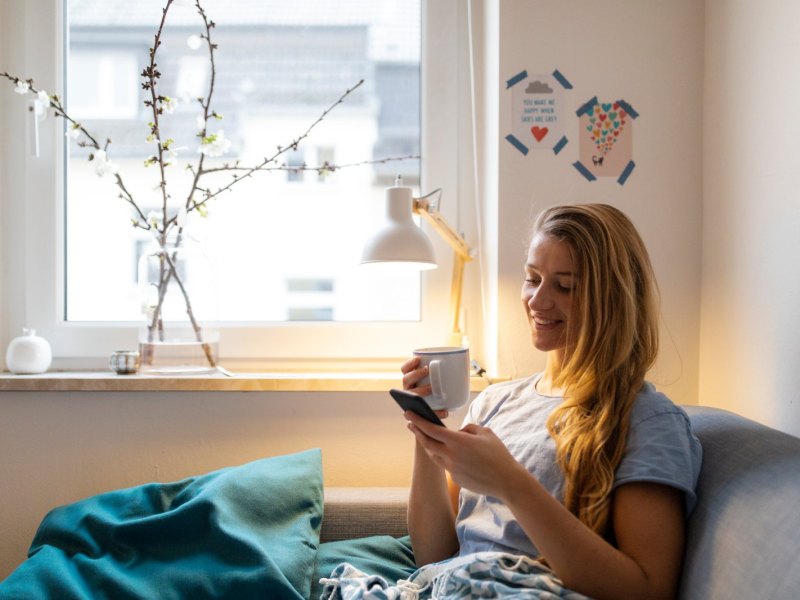 Frau mit Kaffee und Handy in der Hand.