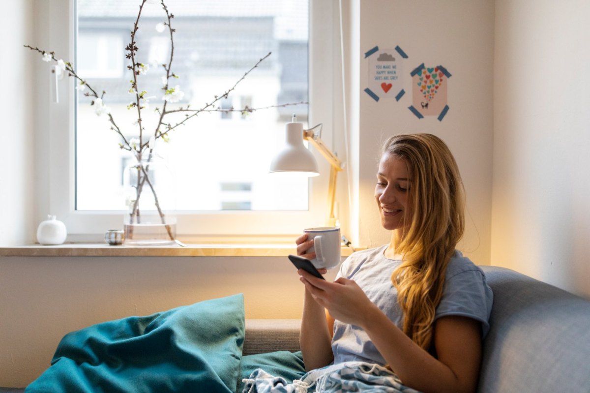 Frau mit Kaffee und Handy in der Hand.