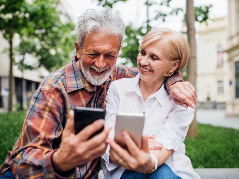 Ein älteres Paar schaut glücklich auf ihre Smartphones.