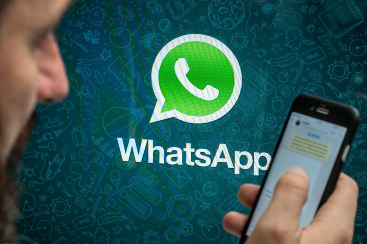 Das WhatsApp-Logo und eine Person mit Smartphone im Vordergrund