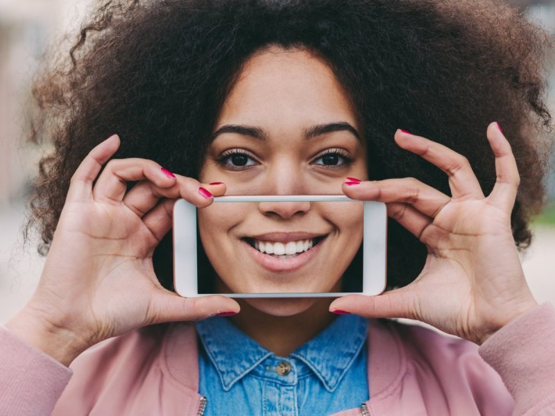 Frau hält Smartphone vor Zähne