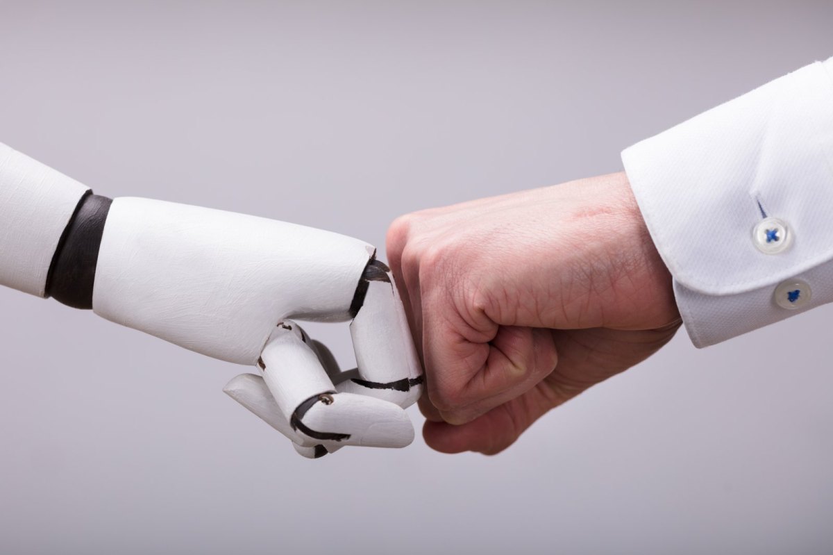 Roboterhand und Menschenhand geben sich eine Faust.