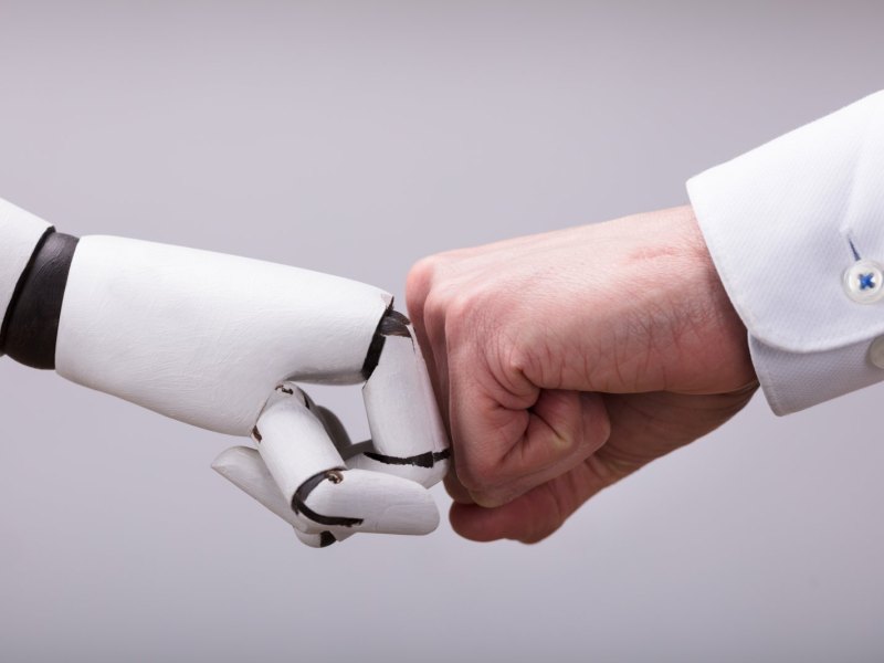Roboterhand und Menschenhand geben sich eine Faust.