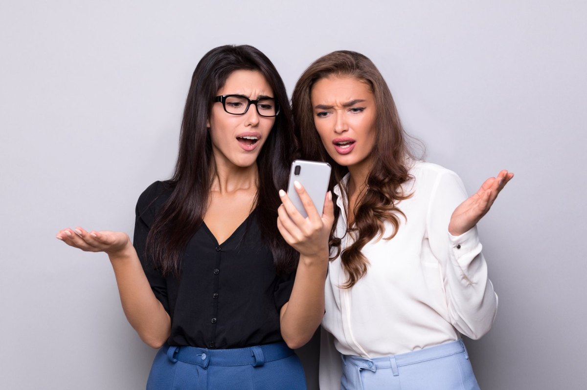 Zwei Frauen blicken irritiert böse auf ein Handy.