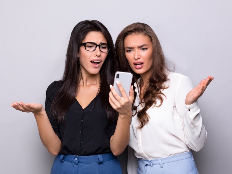 Zwei Frauen blicken irritiert böse auf ein Handy.