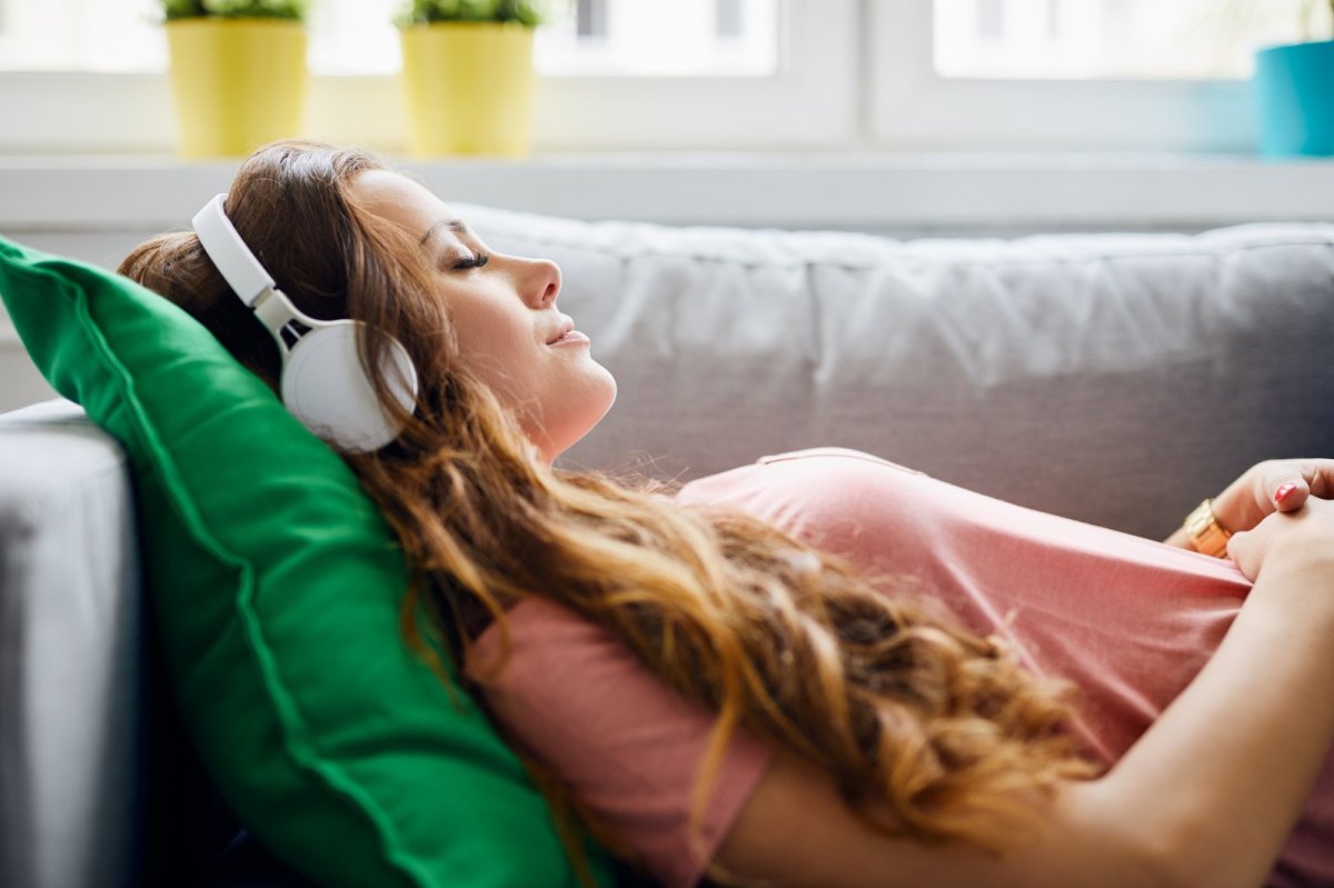 frau liegt mit Kopfhörern auf dem Sofa.