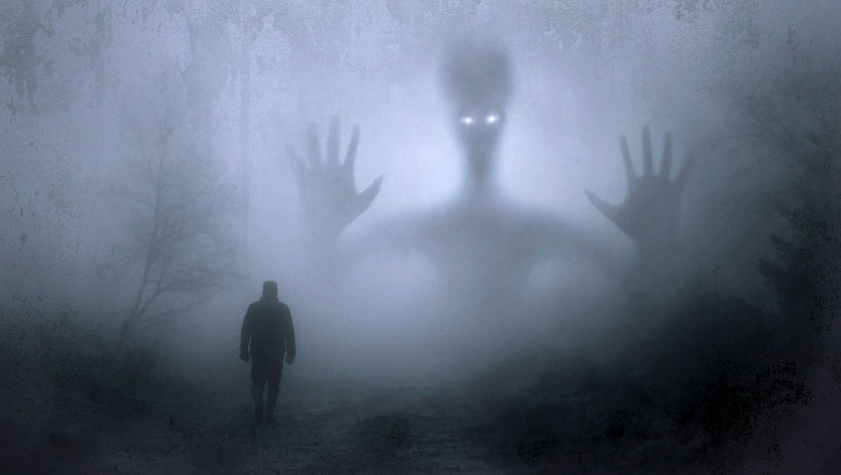 Mensch steht im Nebel vor einer großen Alien-Silhouette.