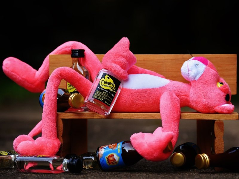Ein Rosarother Panther aus Stoff liegt mit Feigling-Flaschen auf einer Bank.