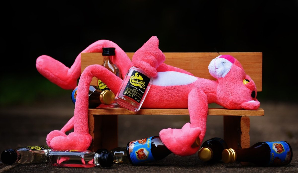 Ein Rosarother Panther aus Stoff liegt mit Feigling-Flaschen auf einer Bank.