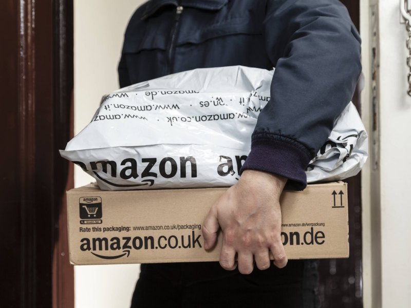 Amazon-Lieferbote hält zwei Pakete im Arm