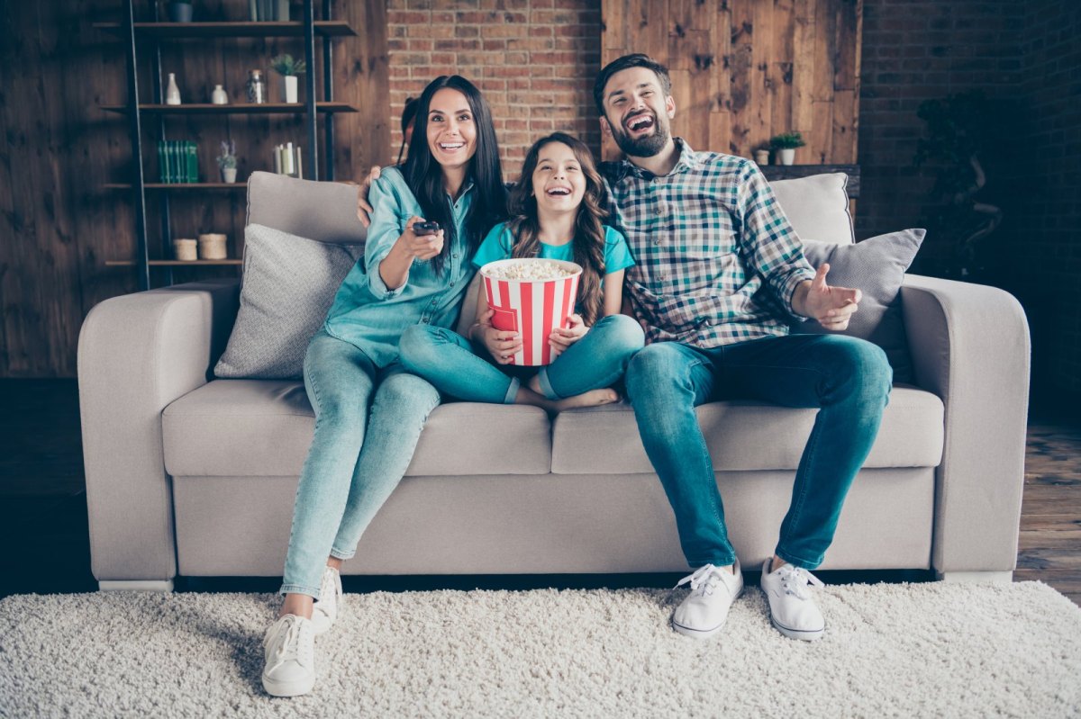 Eine Familie sitzt auf dem Sofa und sieht fröhlich fern.