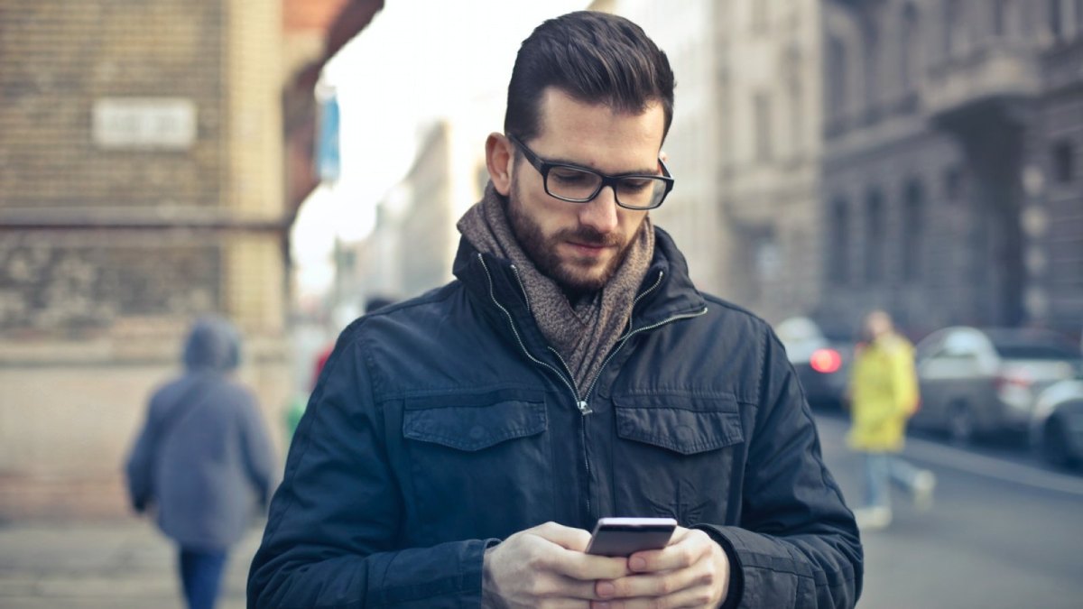 Ein Mann steht auf der Straße und schaut auf sein Smartphone.