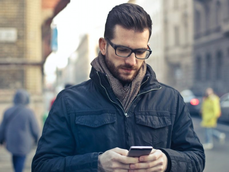 Ein Mann steht auf der Straße und schaut auf sein Smartphone.