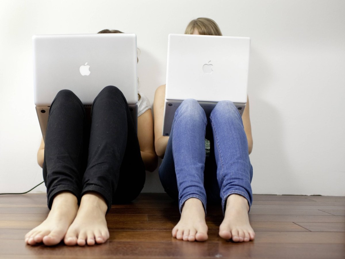 Zwei Frauen sitzen versteckt hinter ihrem Laptop