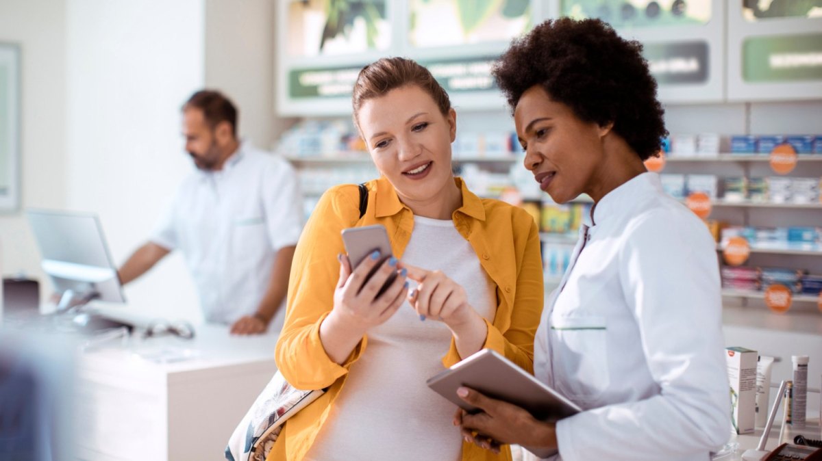 EIne Frau zeigt ihren Smartphone-Bildschirm einer Apothekerin.