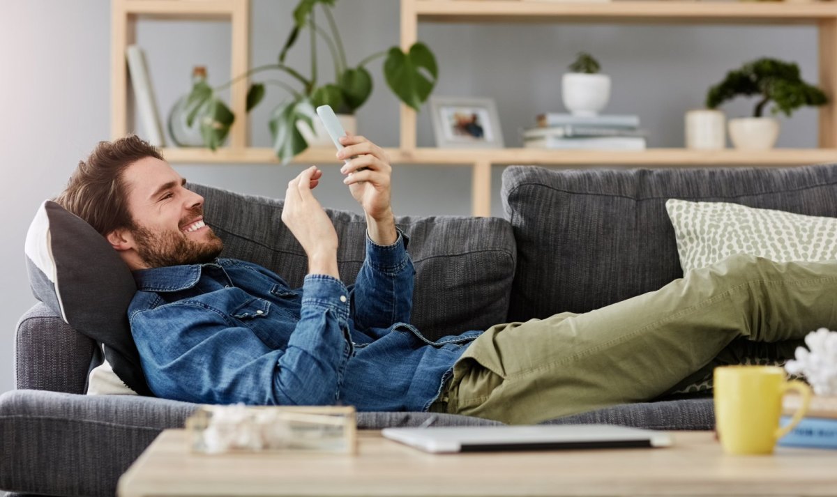 Mann liegt auf dem Sofa und beschäftigt sich mit seinem Handy.