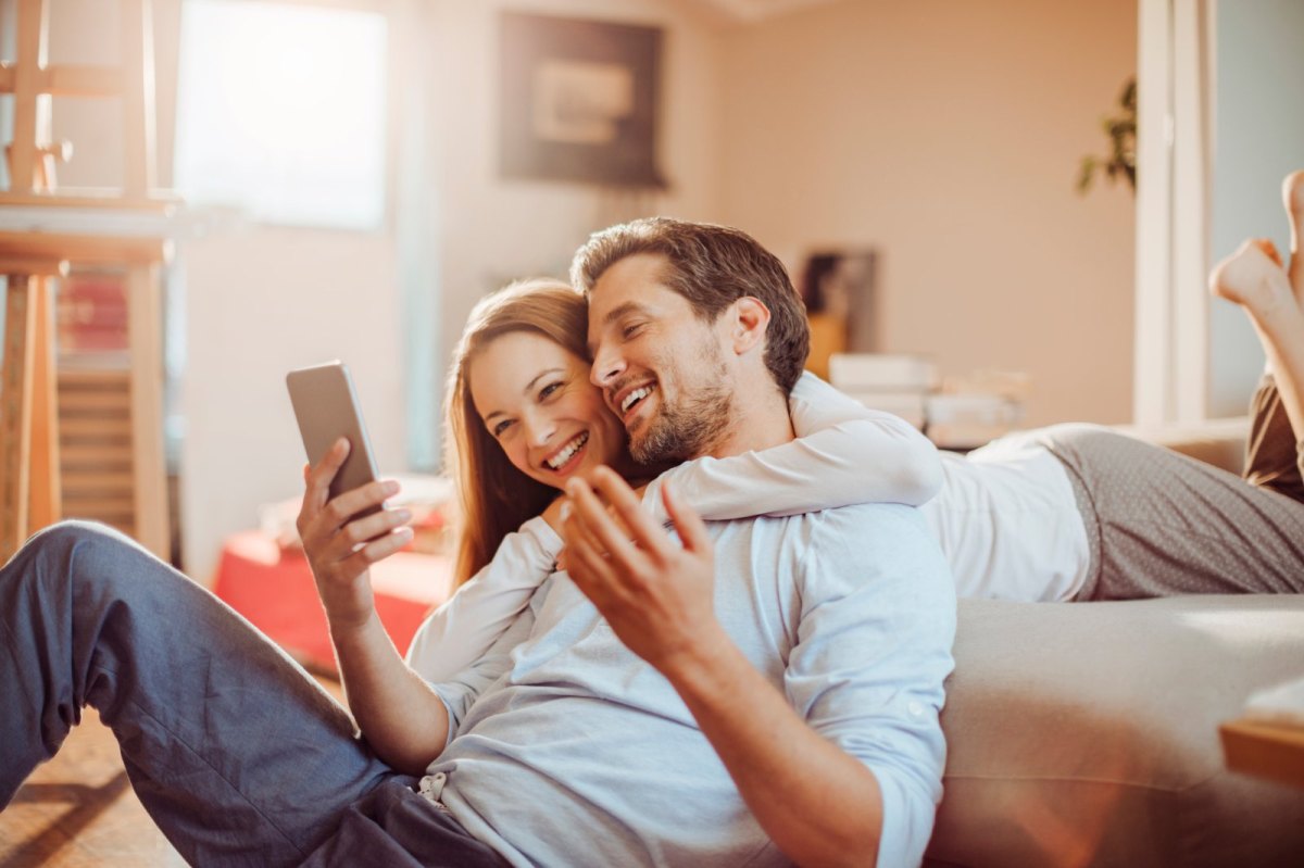 Mann und Frau schauen glücklich auf ein Handy.