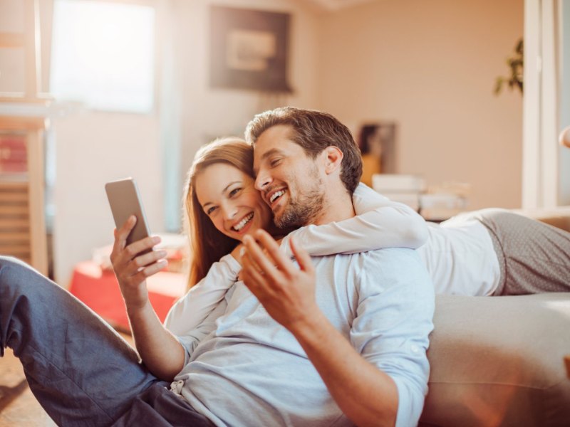 Mann und Frau schauen glücklich auf ein Handy.