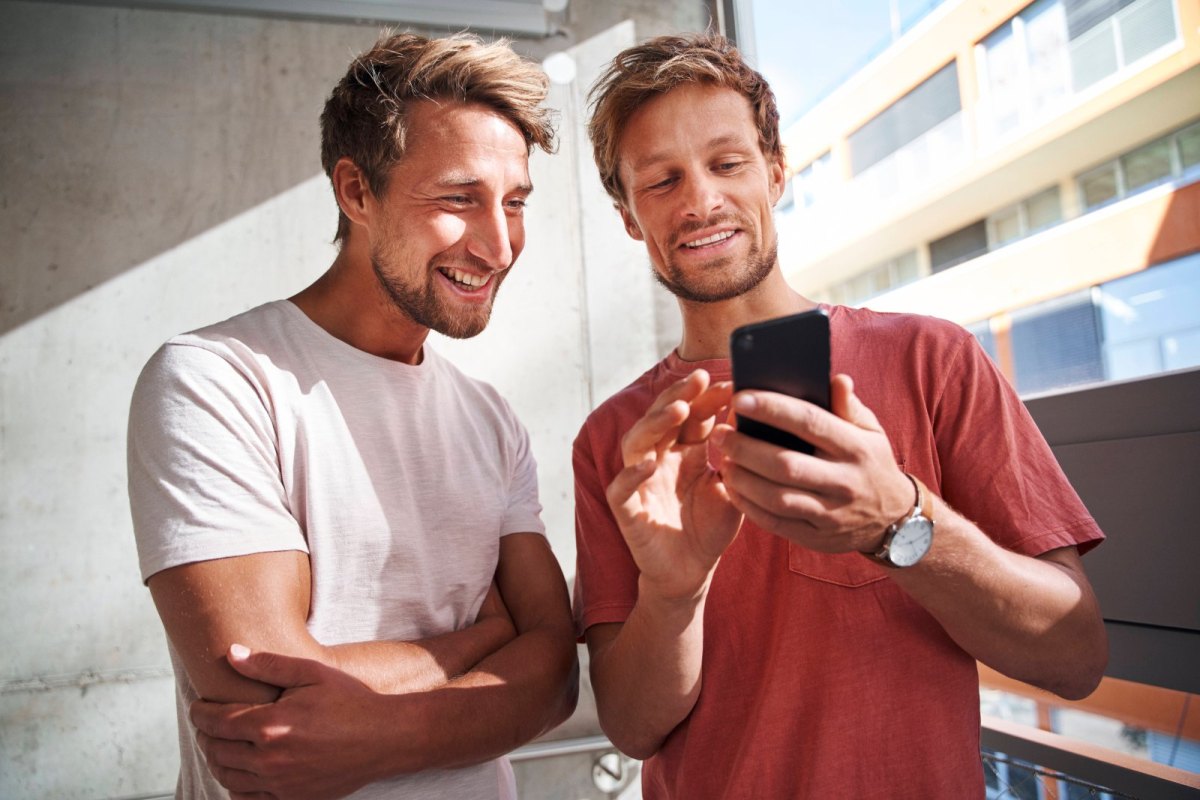 Ein Mann zeigt einem anderem Mann etwas auf seinem Handy.